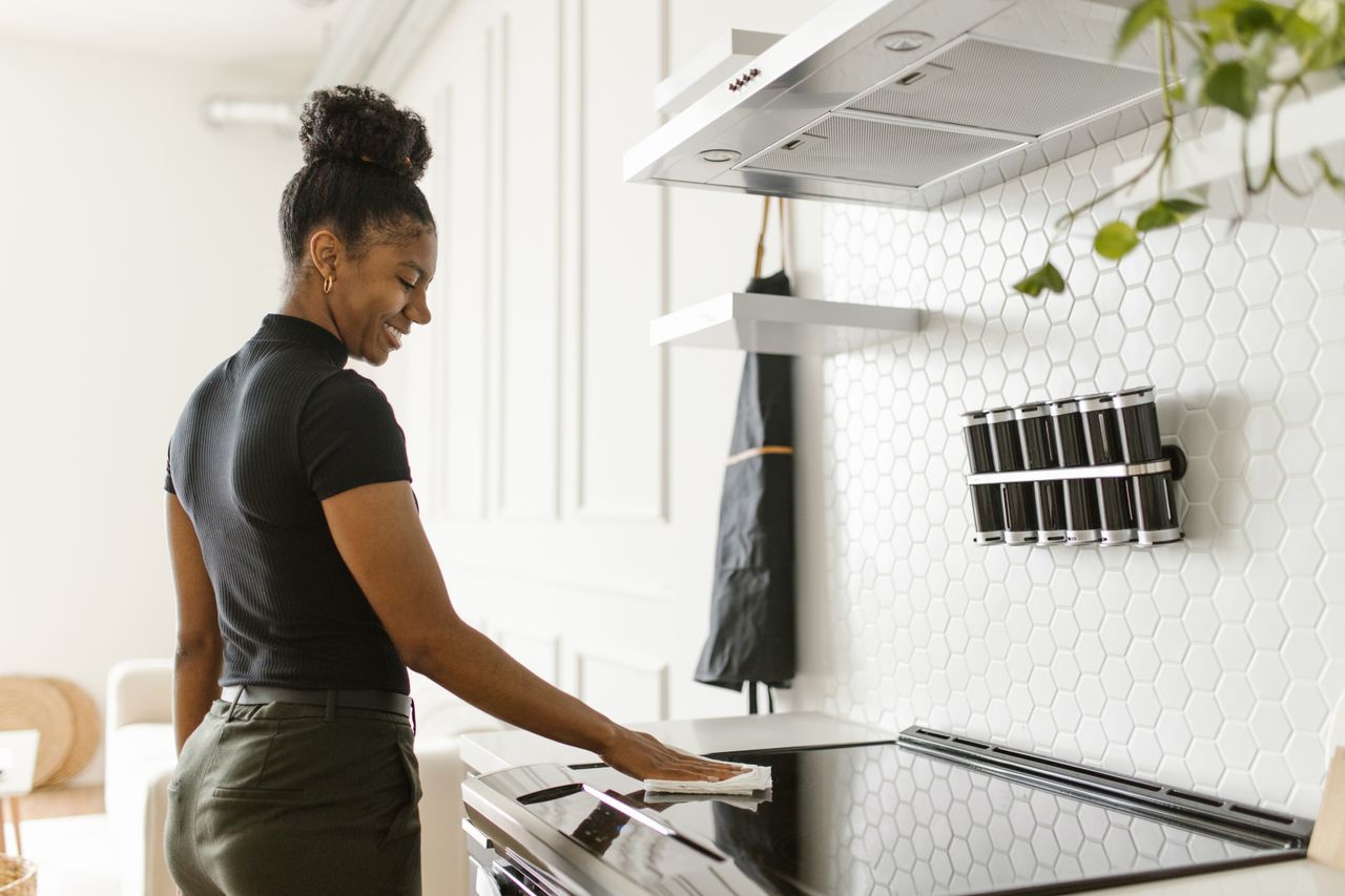 A woman cheerfully cleans her kitchen, focusing on the electric stove in a bright, modern space.