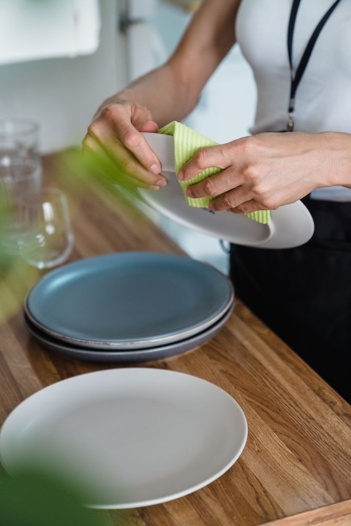 home-img A person cleans a plate with a cloth on a wooden kitchen counter.
